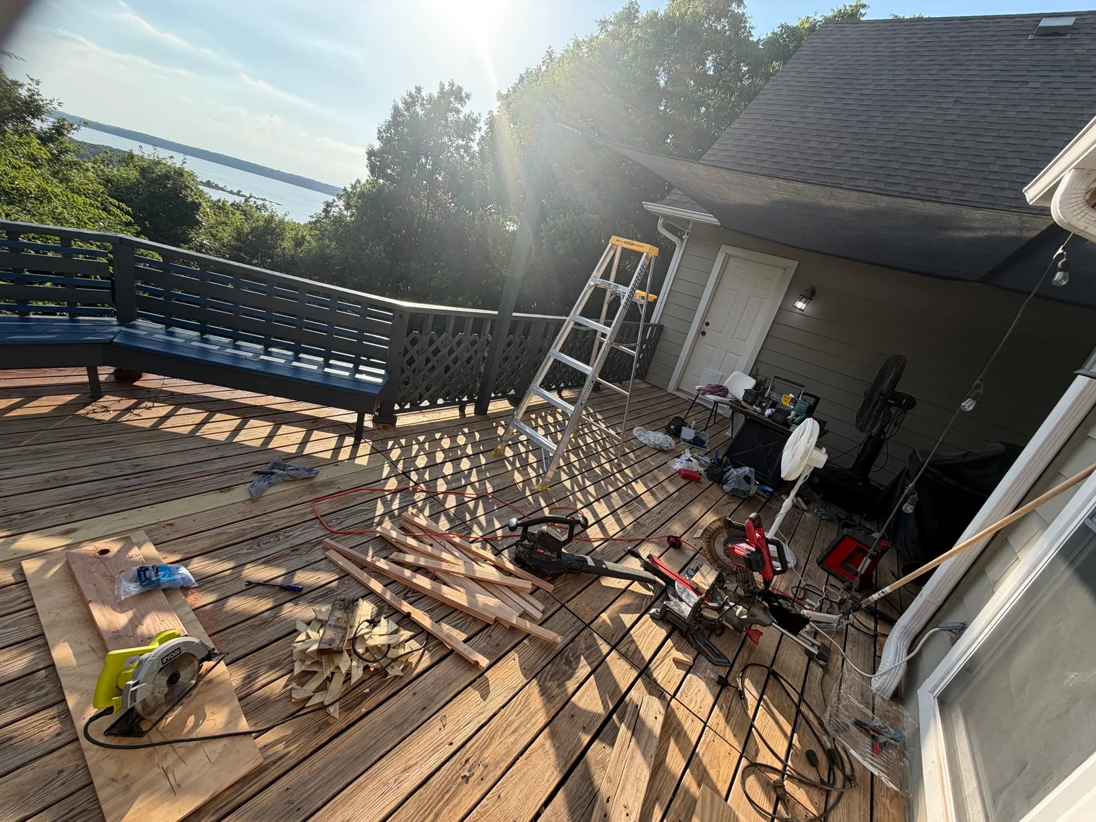 Wooden deck during restoration with sanded surface, blue railing, and preparation equipment
