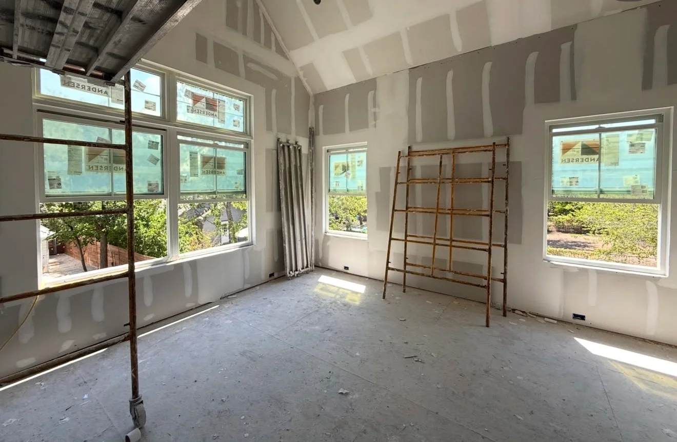 Interior room with taped drywall, vaulted ceiling, and large windows during paint preparation phase