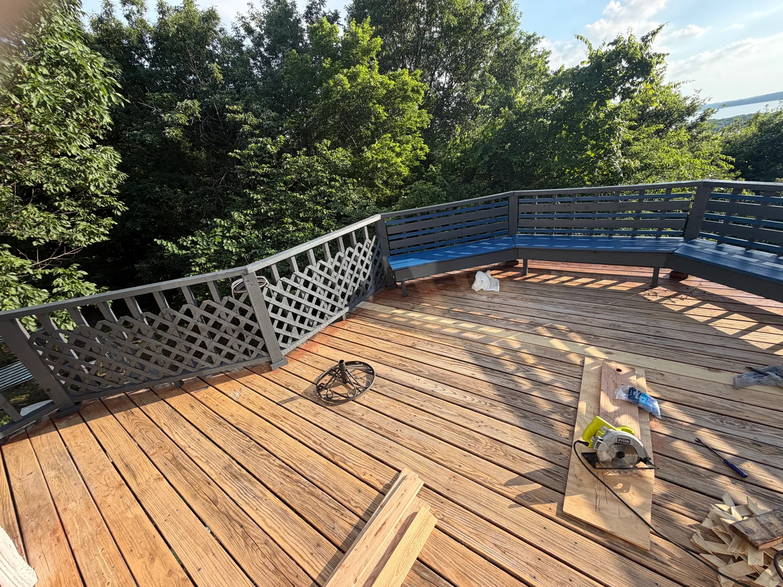 Stained composite deck with painted lattice and blue accent railings overlooking wooded landscape