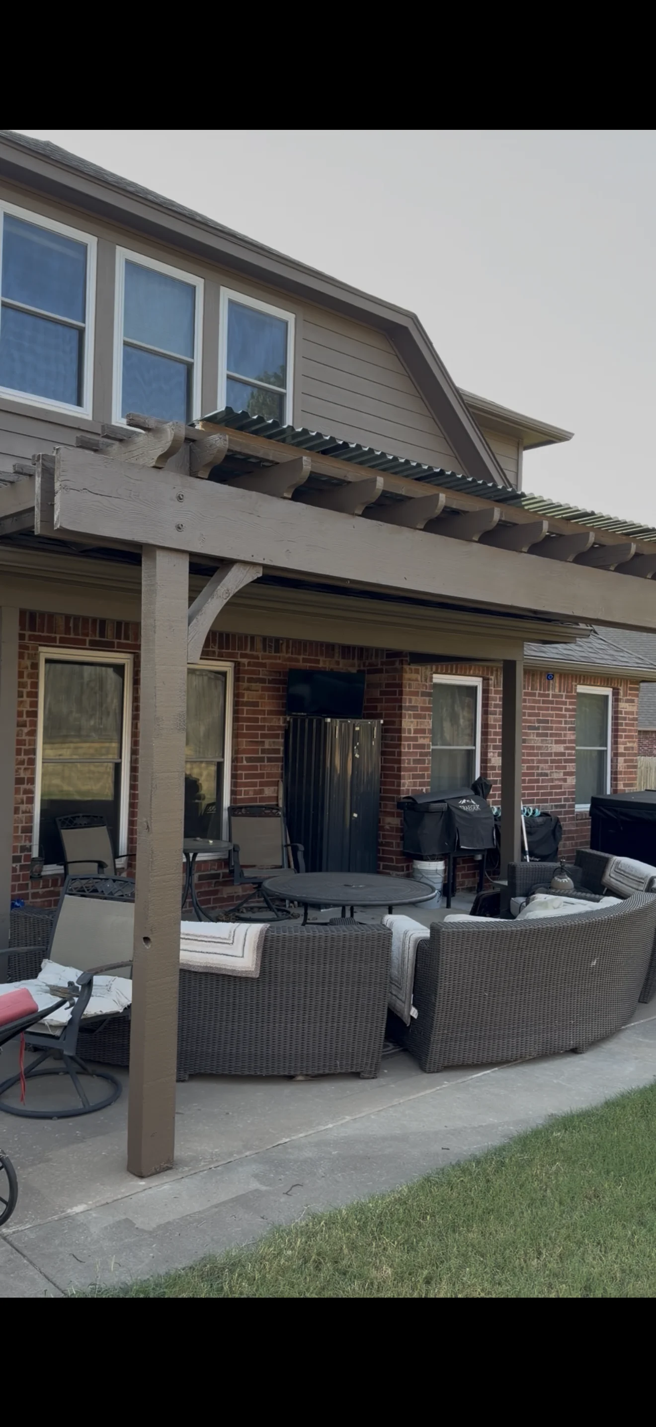 White painted pergola with beam structure over patio, brick house exterior with painted trim and windows
