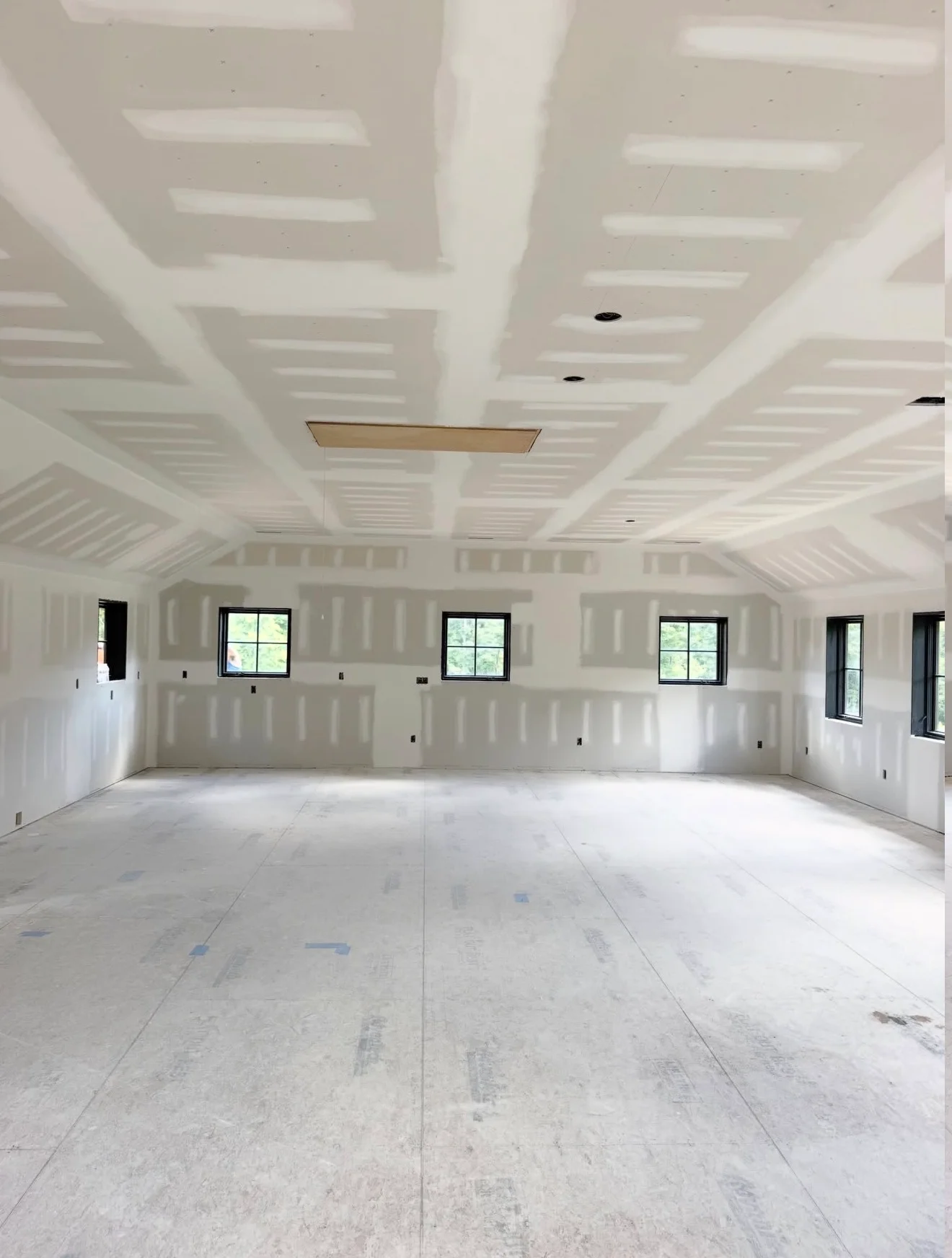 Finished drywall ceiling with coffers and recessed lights, drywall walls with outlet boxes in open room