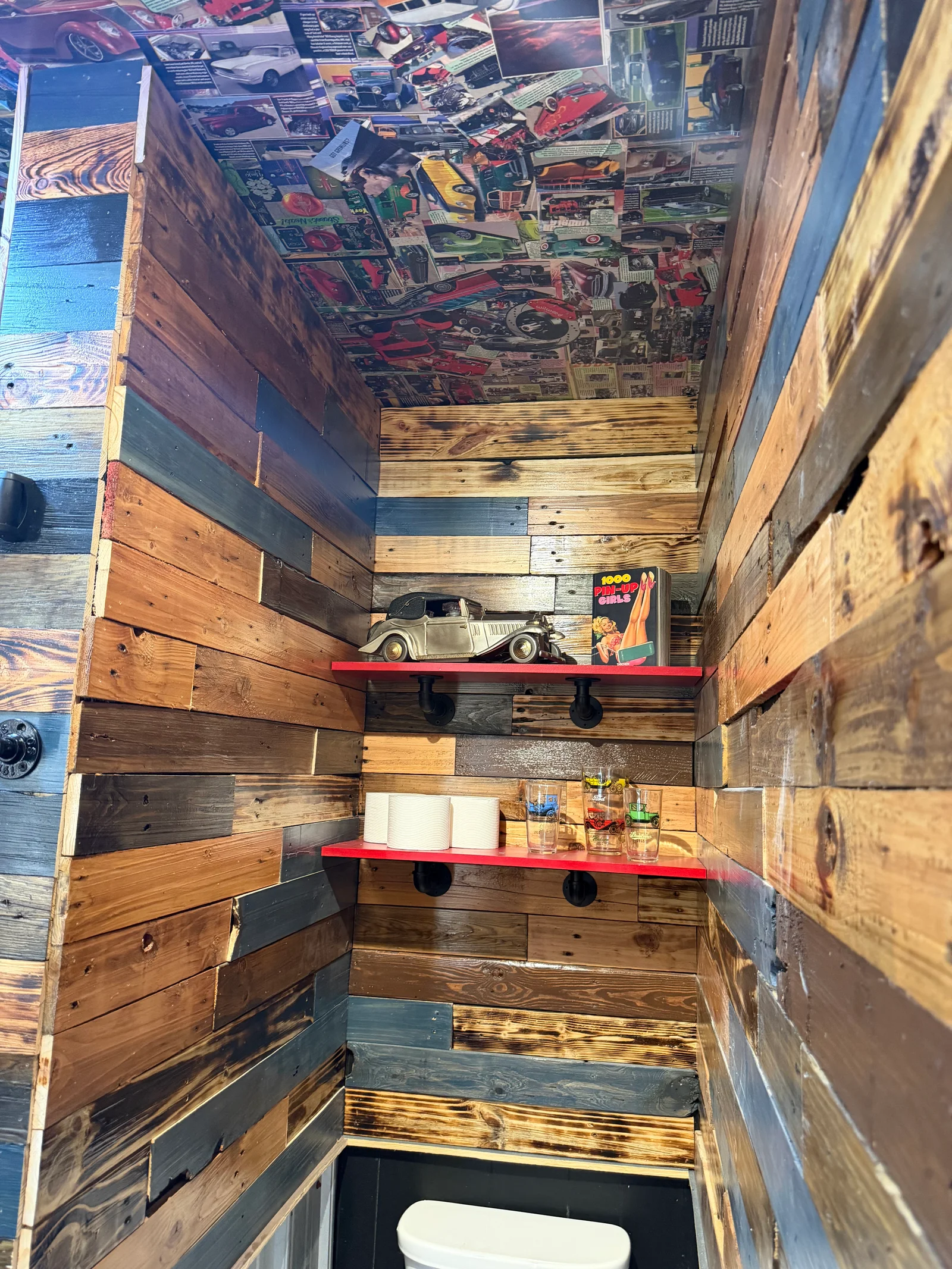 Garage interior with multi-toned reclaimed wood walls, red shelves, and vintage automotive decor
